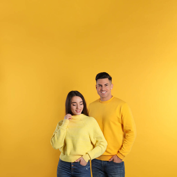 Happy couple wearing warm sweaters on yellow background - Valokuva, kuva