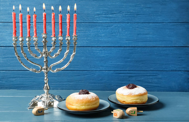 Silver menorah, dreidels with He, Pe, Nun, Gimel letters and sufganiyot on blue wooden table, space for text. Hanukkah symbols - Foto, immagini