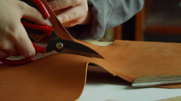 Gros plan slow motion tailleurs ciseaux faire une incision dans un morceau de cuir véritable dans le processus de création de chaussures de créateurs. - Photo, image