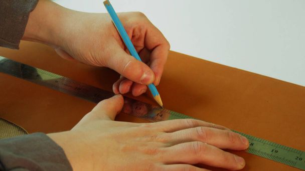 Um sapateiro faz um padrão para botas feitas de couro genuíno. Use um lápis e uma régua para desenhar uma linha reta para o corte. - Foto, Imagem