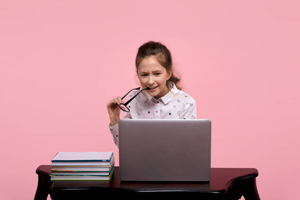 Girl carefully looks at the laptop and holds glasses in the corner of her lips. - Foto, Bild