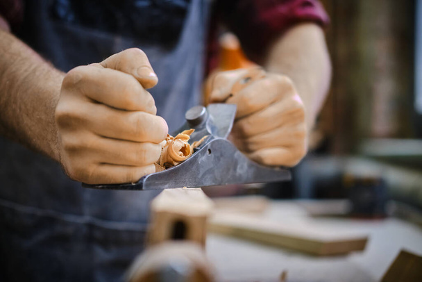 Close up Man hands with carpenters plane on wooden background - 写真・画像