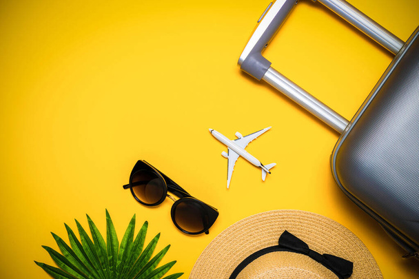 Zomer vakantie poster. Dames accessoires reiziger: koffer, wit vliegtuig, zonnebril op gele achtergrond met lege ruimte voor tekst. Zomervakantie en product reclame concept - Foto, afbeelding