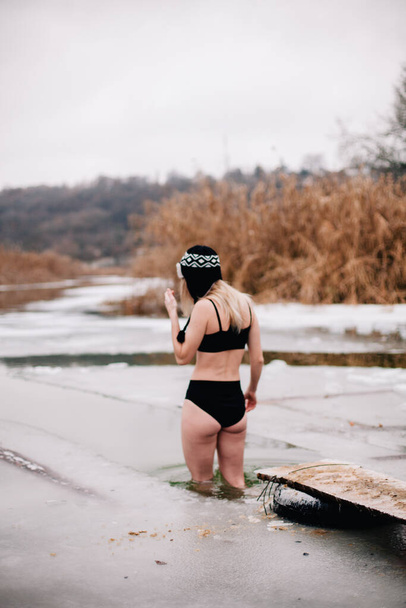 Young slender girl bathes in winter in a river hole - Foto, Imagen
