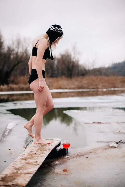 Young slender girl bathes in winter in a river hole - 写真・画像