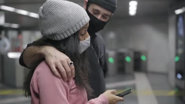 Geschlossene Aufnahme eines jungen gemischtrassigen Paares, das sich in einem Gang der U-Bahn umarmt und über etwas spricht, was sie auf ihrem Smartphone sehen. - Filmmaterial, Video