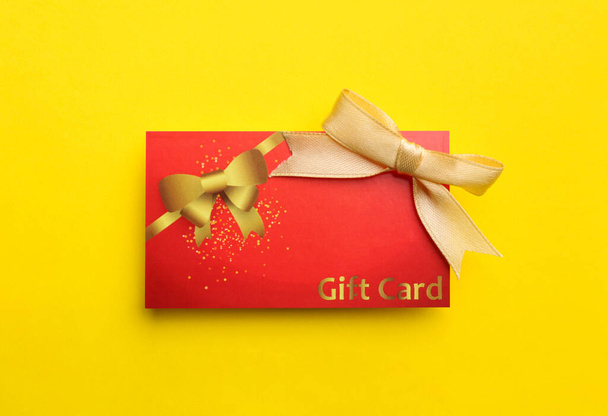 Gift card with bow on yellow background, top view - Zdjęcie, obraz