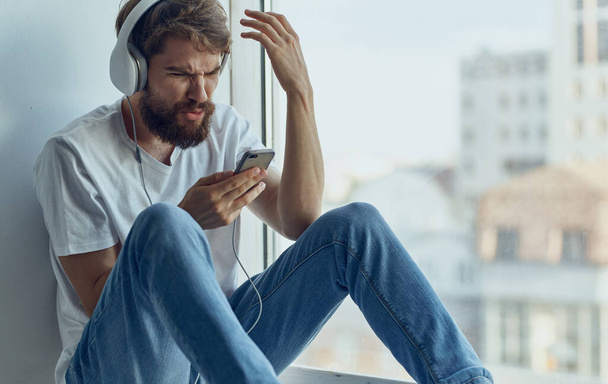 hombre barbudo en auriculares escuchando música cerca de la tecnología de recreación de ventanas - Foto, imagen