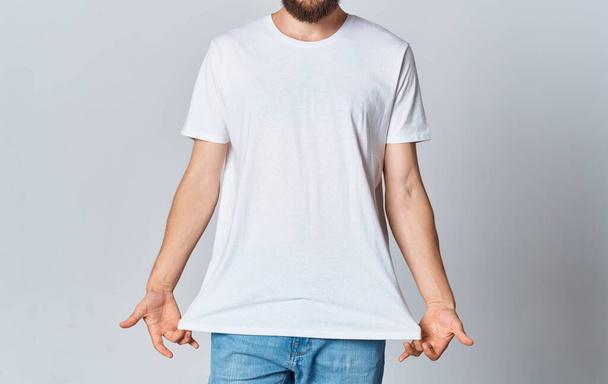 A man in a white T-shirt on a light background gestures with his hands cropped view of jeans Copy Space - 写真・画像