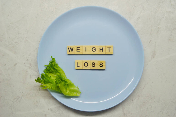Фраза втрати ваги з дерев'яних літер на синій тарілці з листям зеленого салату на світлому дерев'яному фоні
 - Фото, зображення