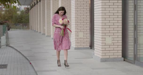 Spiel im schicken gestreiften Kleid glücklich geht nach einem Date mit einem Blumenstrauß - Filmmaterial, Video