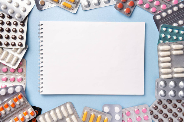 Bunch of pills of different colors in blisters pack on blue background with notebook, copy space. Prescription blank for medicine drug recipe. Pharmacy tablets for treatment of health. - Foto, Imagen