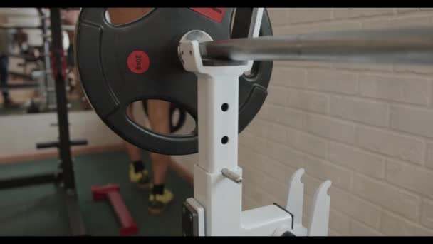Junge Bodybuilderin mit nacktem Oberkörper trainiert im Fitnessstudio und entfernt Pfannkuchen von einer Langhantel, die auf einem Gestell steht - Filmmaterial, Video