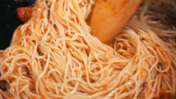 Egy férfi kolbásszal keveri a spagettit egy serpenyőben a tűzhelyen. - Felvétel, videó