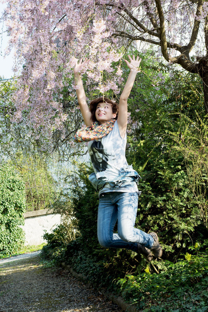 νεαρή γυναίκα χαρούμενη άλματα υπό ανθίζοντας δέντρο - Φωτογραφία, εικόνα