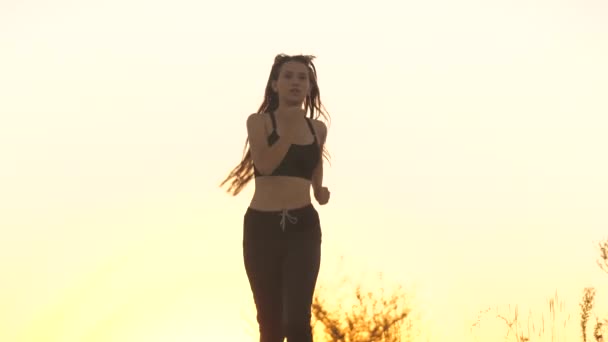 A young sportswoman runs at sunset happy and smiling. Pretty girl runner. Sports activities. The man is doing cross. Love outdoor jogging. Slimming and slim body. Healthy lifestyle. Jumping freedom - Footage, Video