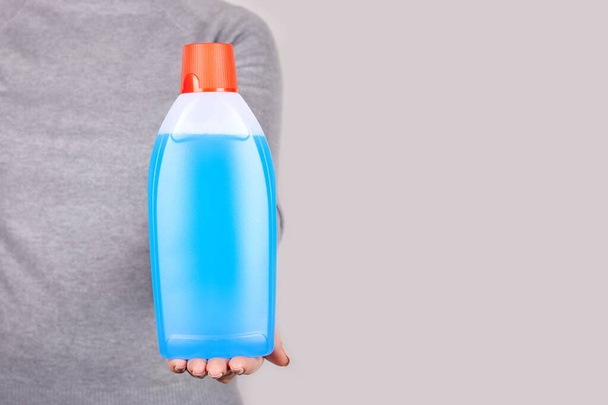 Hand with detergent bottle on grey. - Φωτογραφία, εικόνα
