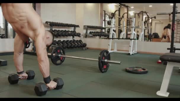 Hombre joven fuerte en pantalones cortos deportivos negros entrenando en el gimnasio y haciendo un soporte de mano apoyado en pesas de metal grandes - Imágenes, Vídeo