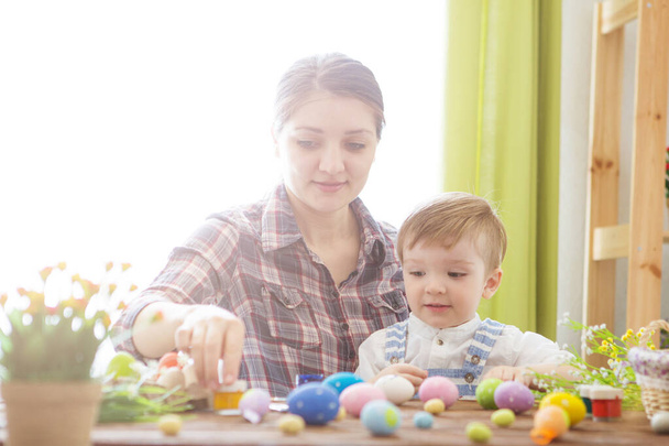 Easter concept. Happy mother and her cute child getting ready for Easter by painting the eggs. Happy family Mom and children son paint easter eggs with colors. Preparation for Easter holiday. - Zdjęcie, obraz