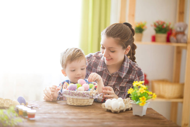 Easter concept. Happy mother and her cute child getting ready for Easter by painting the eggs. - Valokuva, kuva