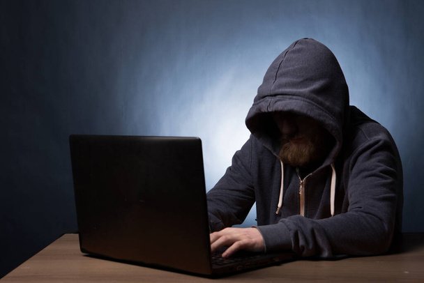 Hooded computer hacker in hood stealing information with laptop - Фото, зображення