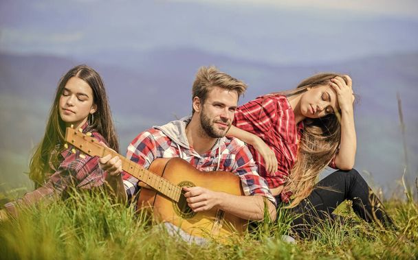 Musical pause. Hiking entertainment. Peaceful place. Melody of nature. Hiking tradition. Friends hiking with music. People relaxing on mountain top while handsome man playing guitar. Singing together - Photo, image