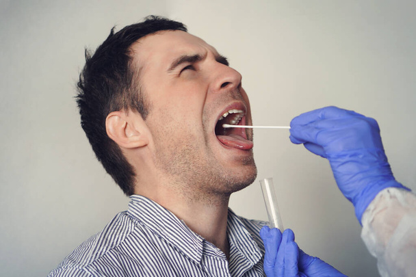 Dokter doet Coronavirus test voor mannelijke patiënt. DNA test. Verzameling van slijm uit de keel voor onderzoek in het laboratorium. Een speekselmonster nemen van een man. PCR polymerasekettingreactie - Foto, afbeelding