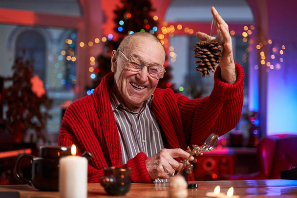 Alegre y feliz hombre viejo haciendo decoración en la mesa en la habitación - Foto, Imagen