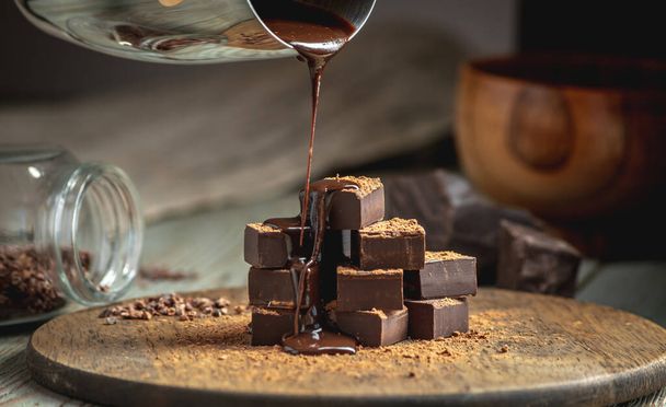 Un mucchio di deliziosi cubetti di cioccolato fondente amaro cosparso di cacao in polvere e versato con cioccolato liquido. - Foto, immagini