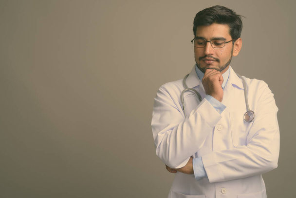 Studio záběr mladý hezký vousatý perský muž lékař nosí brýle na šedém pozadí - Fotografie, Obrázek