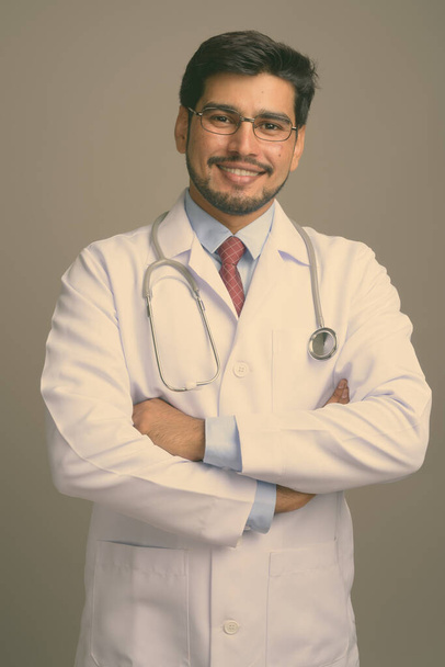 Estudio disparo de joven guapo barbudo médico hombre persa con gafas sobre fondo gris - Foto, Imagen