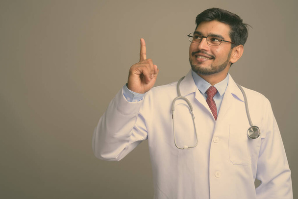 У майстерні молодого вродливого бородатого перського лікаря у окулярах на сірому фоні. - Фото, зображення