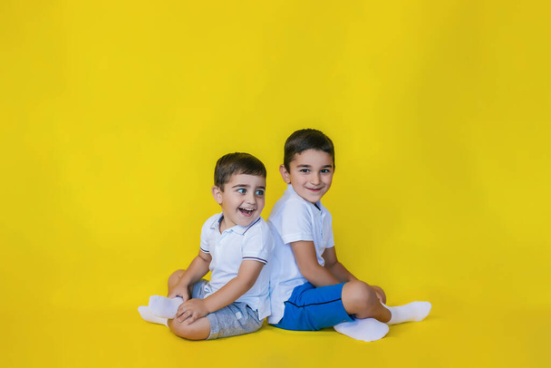 little boys sit on the floor on a yellow background.brothers or friends smile and have fun. Boys of preschool age. - Foto, immagini