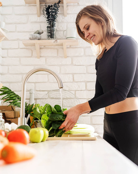 Preparing healthy foods. Young smiling woman in sport clothes washing celery in the kitchen - Foto, Imagen