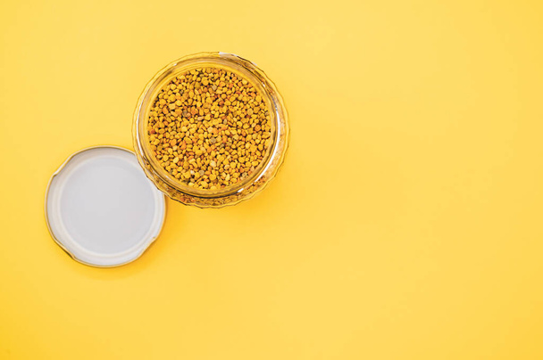 A top view of organic bee pollen in a glass jar next to the lid, placed on a yellow surface - Фото, изображение