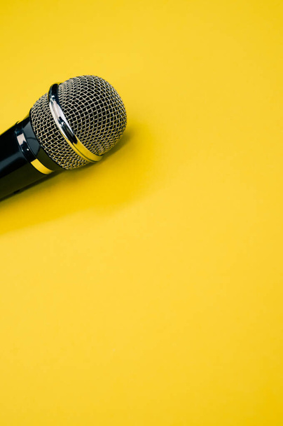 A vertical shot of a microphone on a yellow surface - Фото, изображение