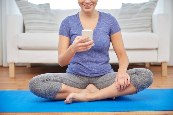 woman with smartphone sitting on mat at home - Photo, Image