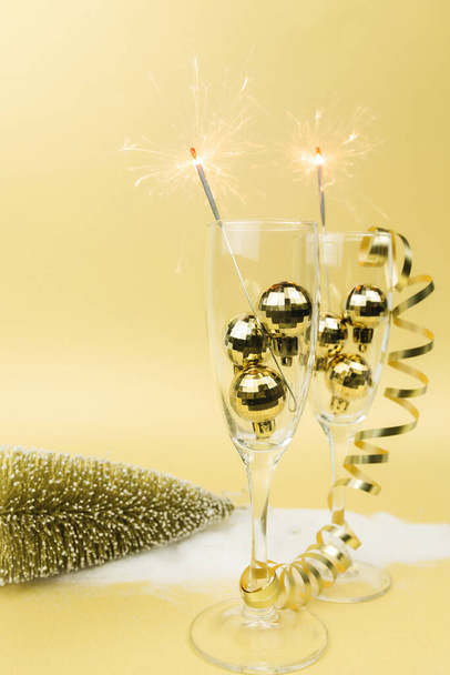 Glasses for sparkling wine, sparklers, christmas tree balls, ribbon, gold background - Photo, Image