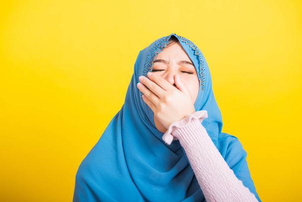 Asian Muslim Arab, Portrait of happy beautiful young woman Islam religious wear veil hijab funny she sleepy yawning wide open mouth hand cover mouth eyes closed studio shot isolated yellow background - Fotó, kép