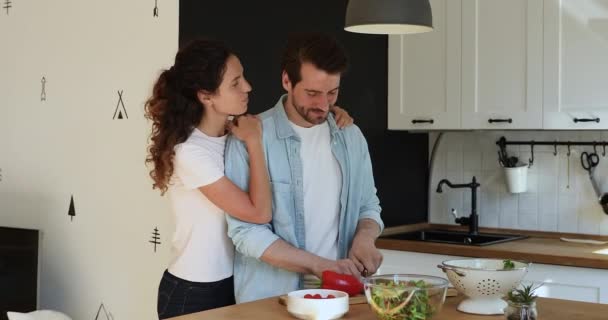 Smiling young woman embracing handsome husband preparing food. - Filmati, video