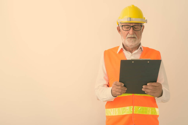 Студійний знімок красивого старшого бородатого працівника будівельника, який читає на кишені під час носіння окулярів на білому тлі
 - Фото, зображення