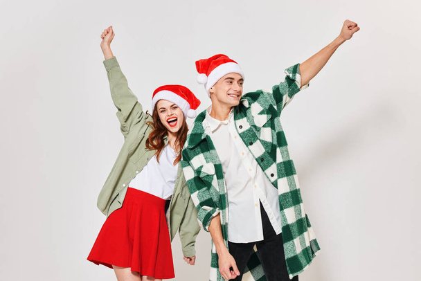Happy loving couple gestures with their hands on a light background and a Christmas hat on their heads - Foto, Imagem