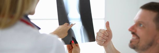 Doctor woman holds an x-ray of leg beside the patient he smiles and shows thumbs up - Foto, Bild