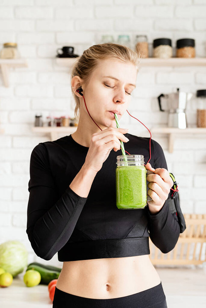 Note di alimentazione, concetto di dieta. Giovane donna bionda che beve frullato verde dal barattolo di muratore a casa cucina - Foto, immagini