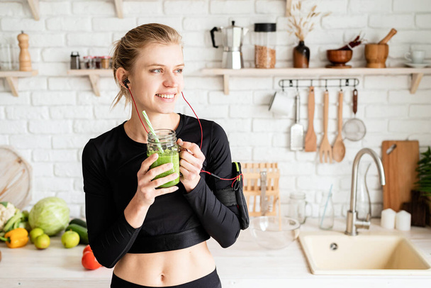 Υγιεινή διατροφή, διαιτητική έννοια. Νεαρή ξανθιά γυναίκα πίνοντας πράσινο smoothie από mason βάζο στο σπίτι κουζίνα - Φωτογραφία, εικόνα