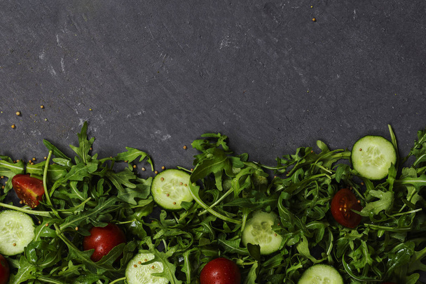 Fresh vegetables arugula, tomato, cucumber, herbs, peppercorns and olives on a gray background. View from above. Place for text, copy space. - Photo, image