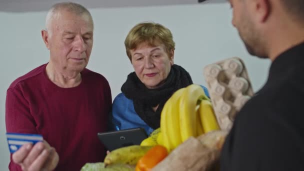 Een bejaarde familie betaalt per creditcard voor koeriersbezorging. Senior online concept en pandemisch concept - Video