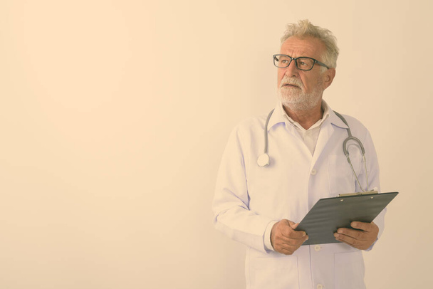 Stúdió lövés jóképű idősebb szakállas férfi orvos gondolkodás közben gazdaság vágólap ellen fehér háttér - Fotó, kép