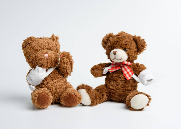 brauner lockiger Teddybär mit umgewickelter Pfote mit weißer Mullbinde auf weißem Hintergrund, Konzept der Verletzungen bei Kindern oder Tieren - Foto, Bild