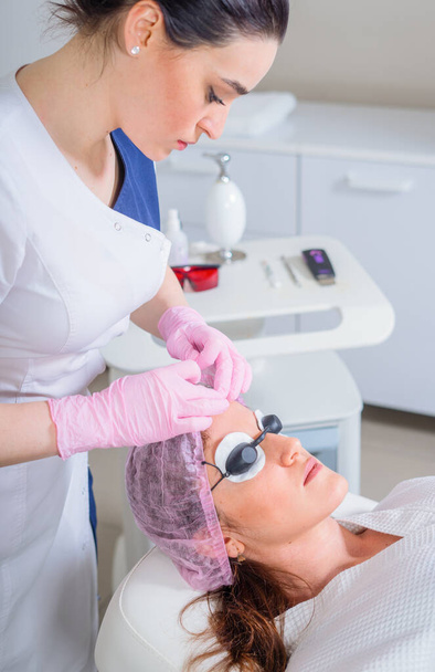 Молодая женщина получает лазерное лечение в косметологической клинике. Глаза, покрытые защитными очками - Фото, изображение